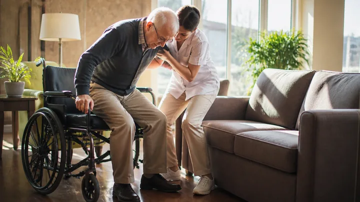 A caregiver helping a man transfer from his wheelchair to a chair